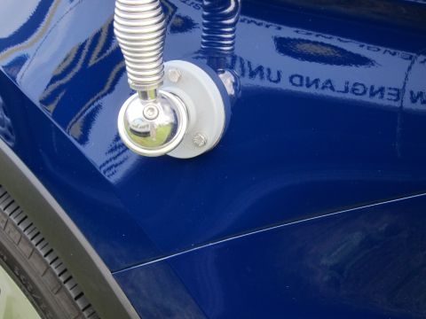 1991 Ford LTD Crown Victoria - close-up of a chrome coil whip-antenna base bolted to a glossy dark blue vehicle body panel reflecting faint lettering.