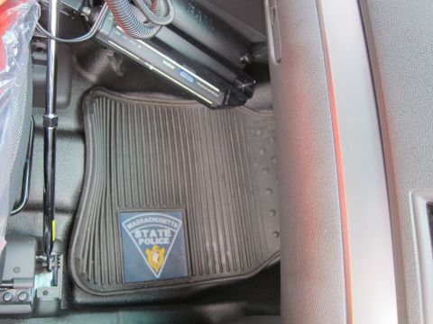 1991 Ford LTD Crown Victoria - Interior front floor of a police vehicle showing a rubber floor mat with a Massachusetts State Police logo and a mounted laptop and cabling.