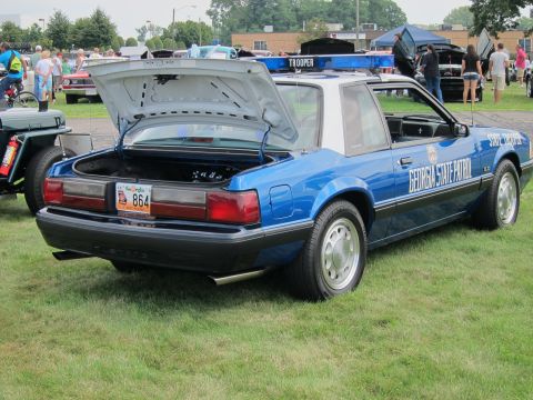 1991 Ford LTD Crown Victoria - blue 1980s-style Ford Mustang notchback marked GEORGIA STATE PATROL, trunk open, displayed on grass at an outdoor car show.