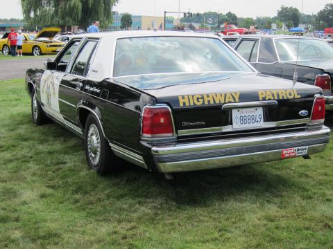 1991 Ford LTD Crown Victoria - black-and-white Ford Crown Victoria sedan marked HIGHWAY PATROL with a California plate, parked on grass at a car show.