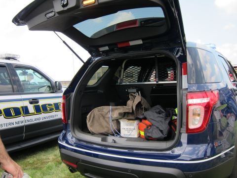 1991 Ford LTD Crown Victoria - open rear cargo area of a dark-blue Ford Explorer police SUV holds duffel bags and equipment, next to a marked POLICE vehicle.