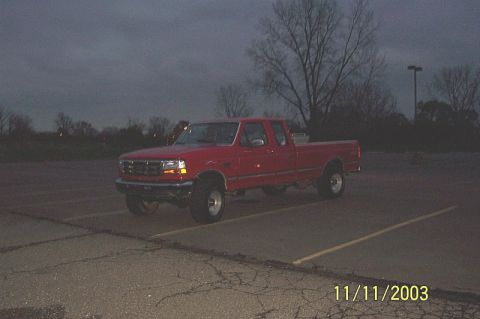 1978 Ford Bronco - This red Ford F-150 pickup truck is parked in a lot under a cloudy sky.