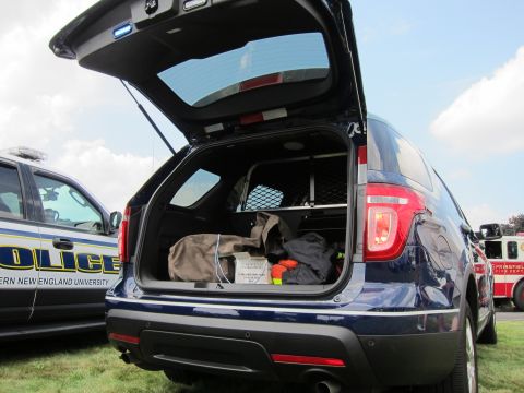 1991 Ford LTD Crown Victoria - dark-blue Ford Explorer police SUV with its rear hatch raised showing a cargo cage and gear, parked beside a university police car.
