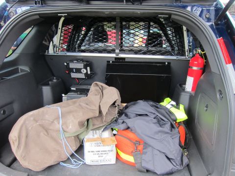 1991 Ford LTD Crown Victoria - Interior cargo area of a police SUV showing a mesh cage partition, a red fire extinguisher, a duffel bag and packed equipment.
