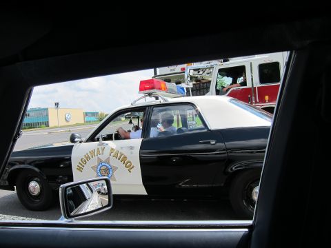 1991 Ford LTD Crown Victoria - Framed by a vehicle window, a black-and-white California Highway Patrol sedan drives alongside a red fire truck on a city street.