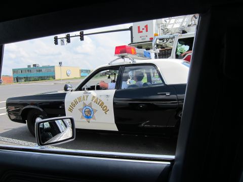 1991 Ford LTD Crown Victoria - Seen through a car window, a black-and-white Highway Patrol sedan with its seven-star door shield sits beside a ladder fire truck at a ligh…