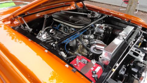 1964 Ford Fairlane - The engine bay of an orange car features a Cobra engine with chrome accents and a red battery.