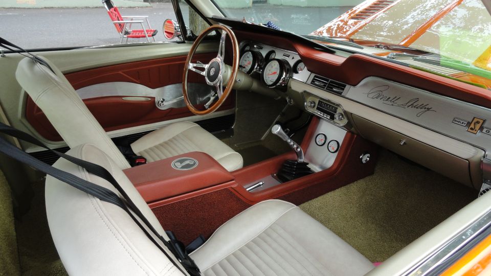 Car interior with white seats, wood steering wheel, and 'Carroll Shelby' script on the dashboard