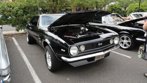 1964 Ford Fairlane - A black Chevrolet Camaro SS is parked with its hood open, revealing the engine, next to another black car.