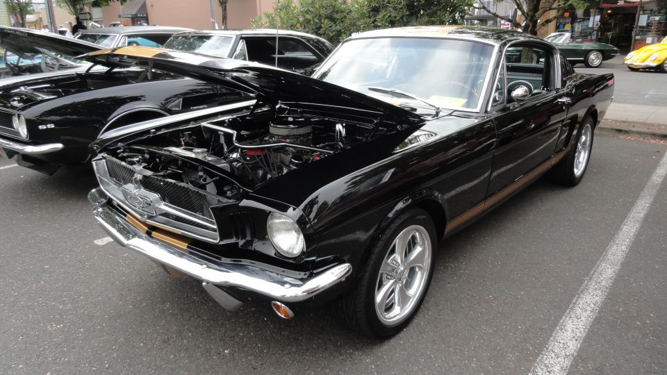 Black 1965 Ford Mustang with hood open, parked next to another classic car