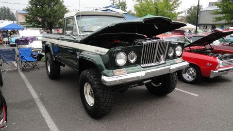1964 Ford Fairlane - A green 1963 Jeep Gladiator pickup truck is displayed with its hood open, alongside other vehicles.