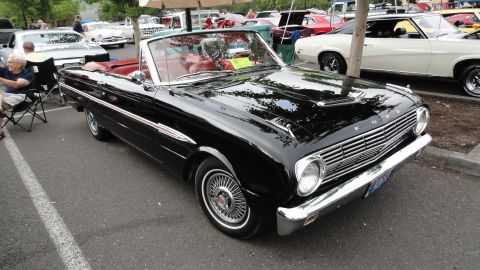 1964 Ford Fairlane - A black 1964 Ford Fairlane convertible is parked at an outdoor event with other vehicles visible.