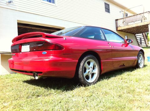 1994 Ford Probe - A red 1994 Ford Probe coupe is shown from the rear 3/4 angle, parked on grass beside a residential building.