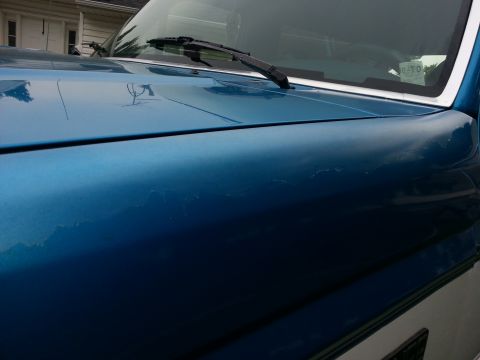 1994 Ford Bronco - Close-up of a blue SUV's hood and windshield, revealing peeling paint and a windshield wiper.