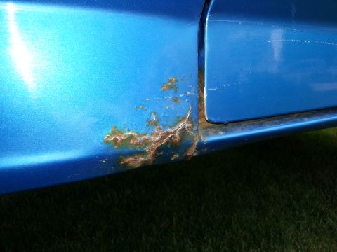 1994 Ford Bronco - This close-up shows significant rust damage on the lower panel of a blue vehicle.