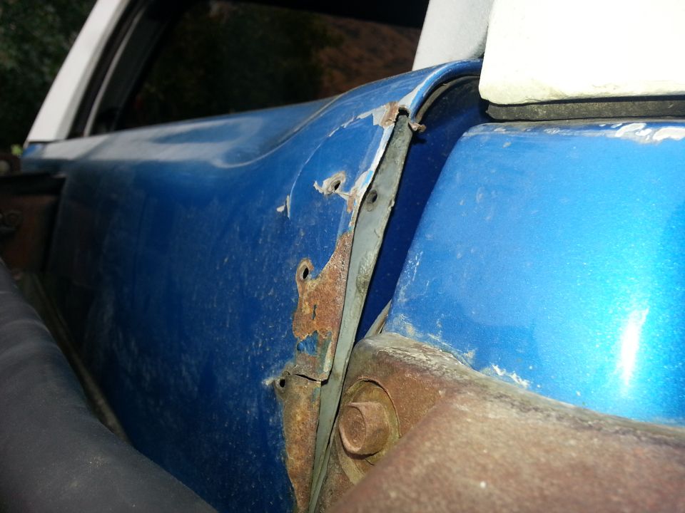 Close-up of rusted metal and blue paint on a vehicle's door hinge area