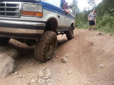 1994 Ford Bronco - A blue and white 1994 Ford Bronco navigates a challenging off-road trail with large tires.