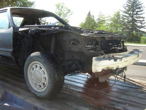 1987 Ford Mustang - Front view of a 1987 Ford Mustang chassis being transported on a flatbed trailer.