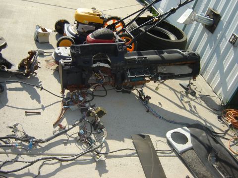 1987 Ford Mustang - A disassembled car dashboard and wiring harness lie on a concrete surface, with lawnmowers and tires nearby.