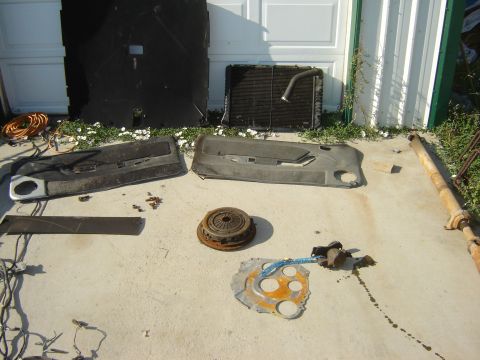 1987 Ford Mustang - Various car parts, such as door panels, a radiator, and a driveshaft, are displayed on a concrete surface.