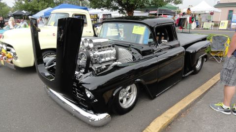 1964 Ford Fairlane - A heavily modified black pickup truck with an exposed engine sits at an outdoor event next to a cream-colored truck.