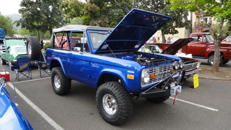 Blue Ford Bronco with hood open, spare tire mounted on rear, off-road tires, aftermarket bumper with winch