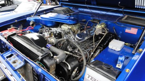 1964 Ford Fairlane - The detailed engine bay of a vehicle, painted in vibrant blue with polished chrome components and an American flag decal on the inner fende…