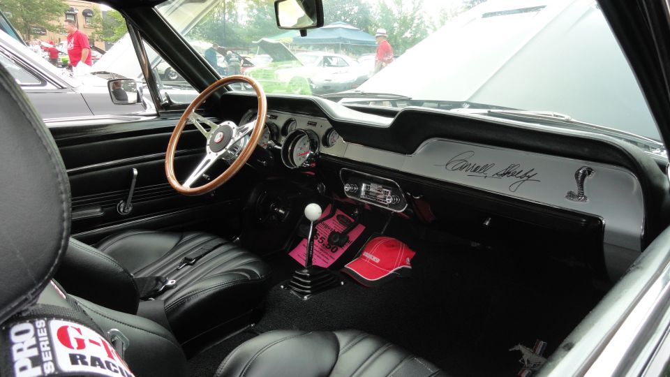 Interior of a 1967 Shelby GT500 with wood steering wheel, racing seats, and 'Carroll Shelby' script on the dash