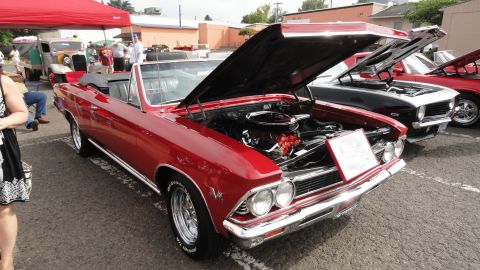 1964 Ford Fairlane - Red convertible at a car show, hood open revealing the engine bay. Other cars are parked nearby.