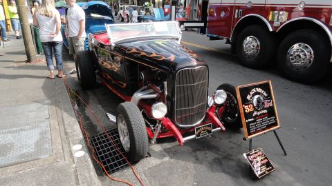 1964 Ford Fairlane - A custom hot rod with flame decals is parked on the street next to a fire truck.