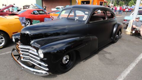 1964 Ford Fairlane - A black hot rod coupe is parked at a car show with other vehicles around it.