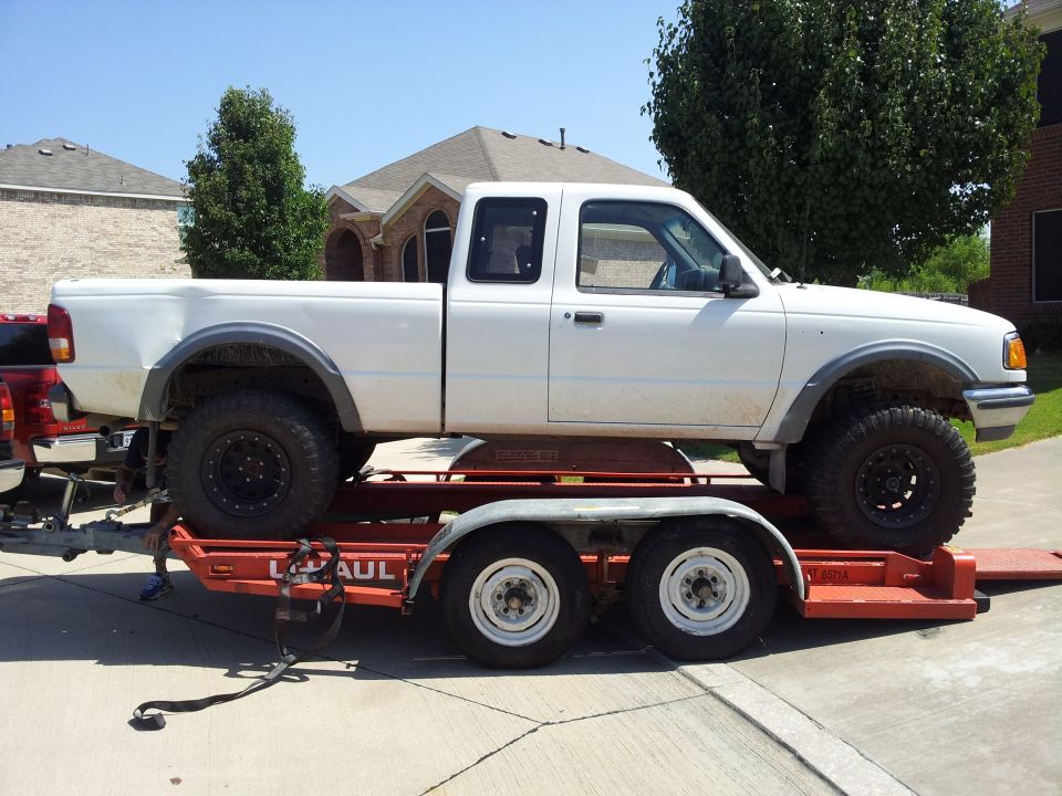 White pickup truck on a U-Haul trailer. Red truck visible behind it