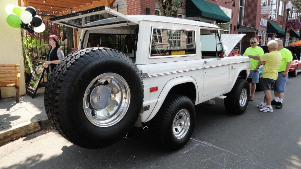 White Ford Bronco with large spare tire, rear-mounted. Open tailgate and hood