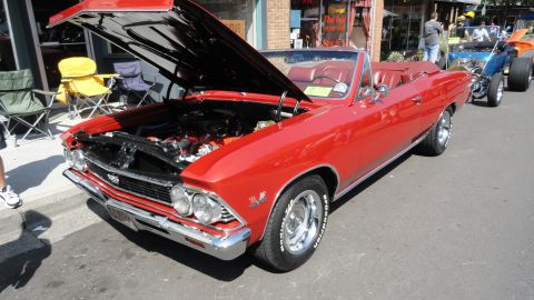 1964 Ford Fairlane - A red convertible with its hood up is parked on a street, with other vehicles visible in the background.