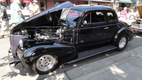 1964 Ford Fairlane - A black coupe hot rod is parked with its hood open, revealing the engine and front grille.