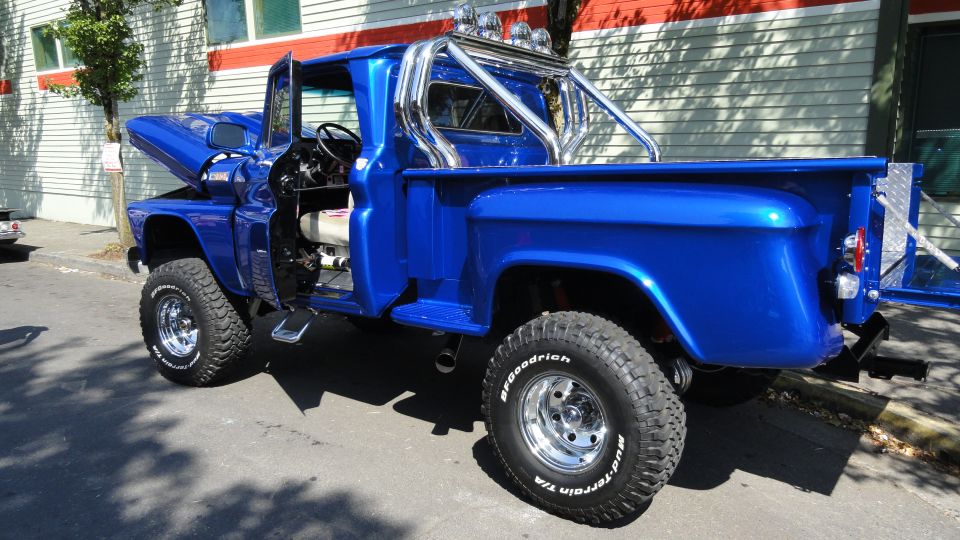 Blue pickup truck, lifted with off-road tires and chrome roll bar. Hood and driver's door are open