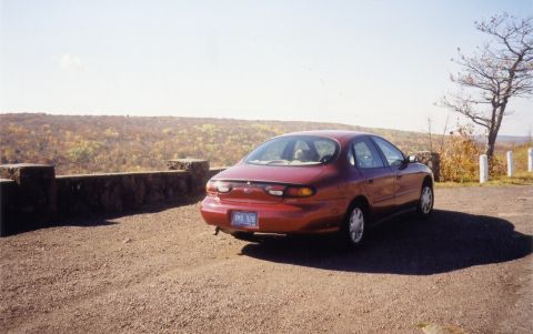 1997 Ford Taurus - Rear view of a red sedan parked at an overlook with a scenic autumn landscape.