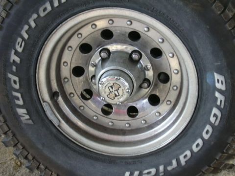 1991 Ford Bronco - Head-on close-up of a polished aluminum eight-hole wheel with a simulated beadlock ring, wearing a BFGoodrich Mud-Terrain white-letter tire…