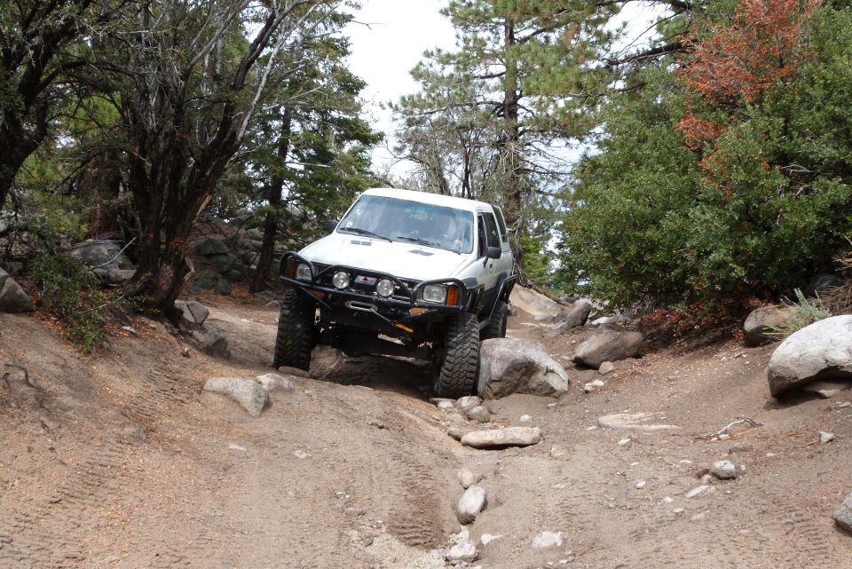 White Toyota 4Runner with aftermarket bumper and off-road tires navigating a steep, rocky trail