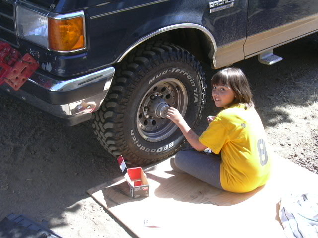 Kid servicing front hub on dark blue Ford Bronco with BFGoodrich Mud-Terrain tires