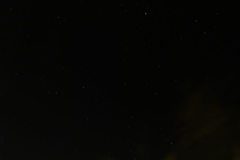 night sky full of stars, with a faint glow on the horizon and a website watermark