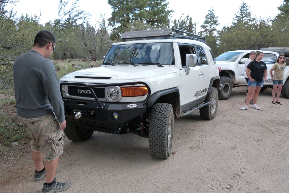 White Toyota FJ Cruiser with aftermarket bumper and roof rack, parked on dirt road