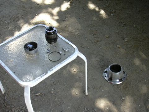 1991 Ford Bronco - Disassembled front-axle hardware laid out on a glass patio table outdoors, a wheel bearing/spindle assembly, a chrome cap, a snap ring, and…
