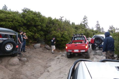 1985 Toyota 4Runner - A group of off-road vehicles are seen on a trail with dense foliage and rocky terrain.