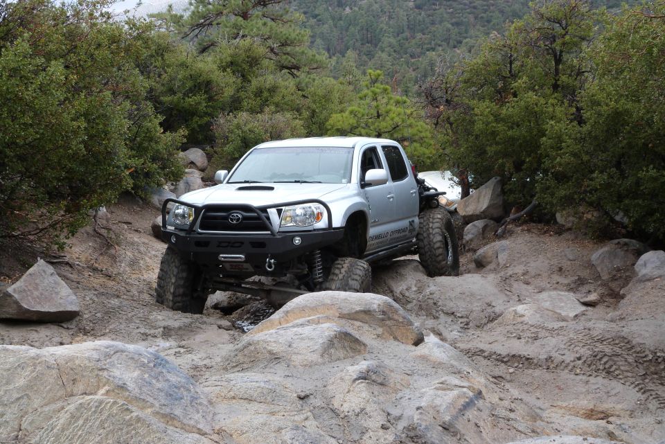Silver Toyota Tacoma with aftermarket bumper and large tires navigating rocky terrain