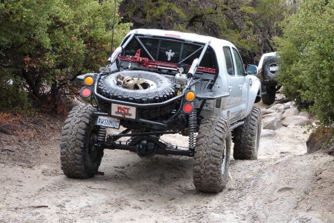 1985 Toyota 4Runner - Modified Toyota Tacoma pickup truck navigates a rocky off-road trail with a spare tire and jack mounted.