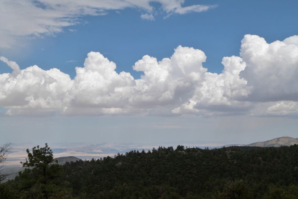 Wide view of cumulus clouds over a forested mountain range and distant hazy landscape