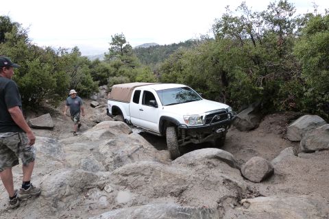 1985 Toyota 4Runner - A white Toyota Tacoma navigates a challenging rocky off-road trail with two people observing.