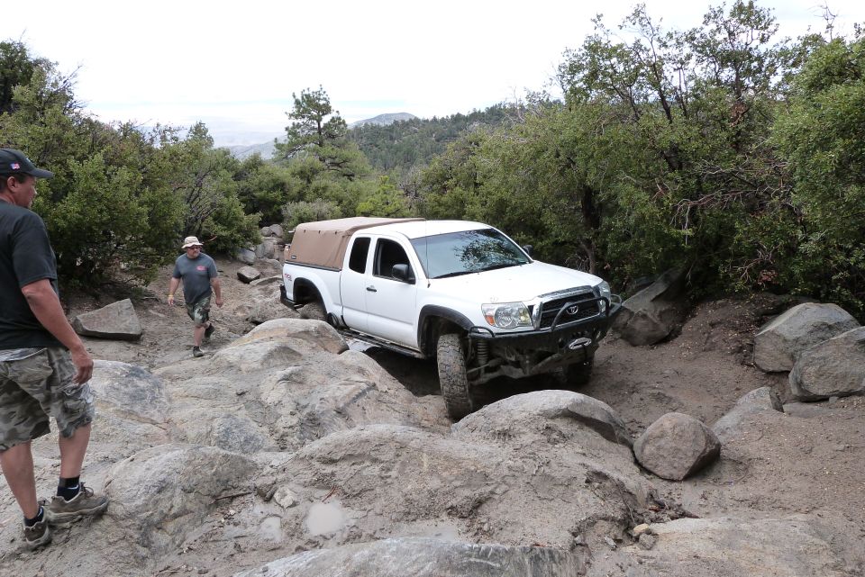 White Toyota Tacoma pickup truck with a tan soft top navigating a rocky trail