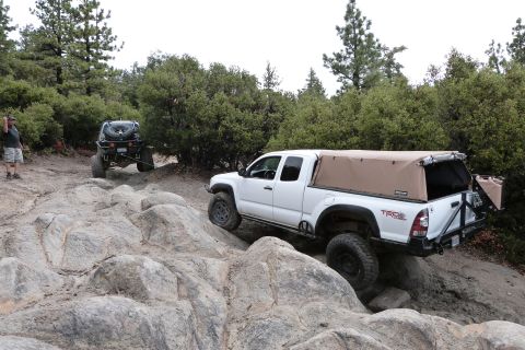 1985 Toyota 4Runner - Two off-road vehicles navigate a rocky trail in a wooded area.